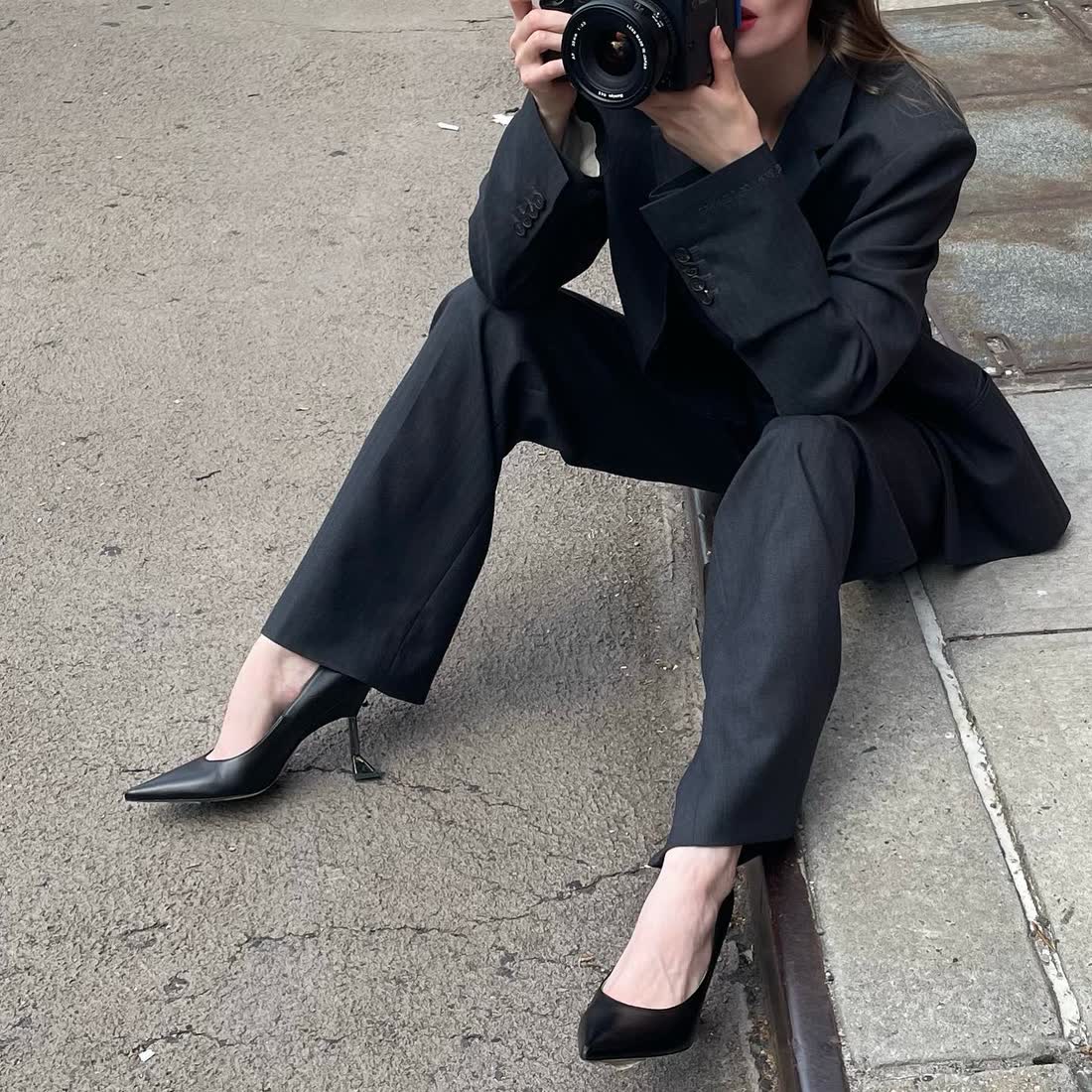 Anastasiia Koval seated in a suit with a camera raised toward the lens.