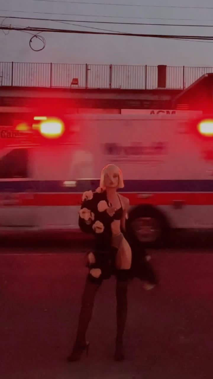 Anastasiia Koval in a black jacket and lace, standing in red light on a city street at night.