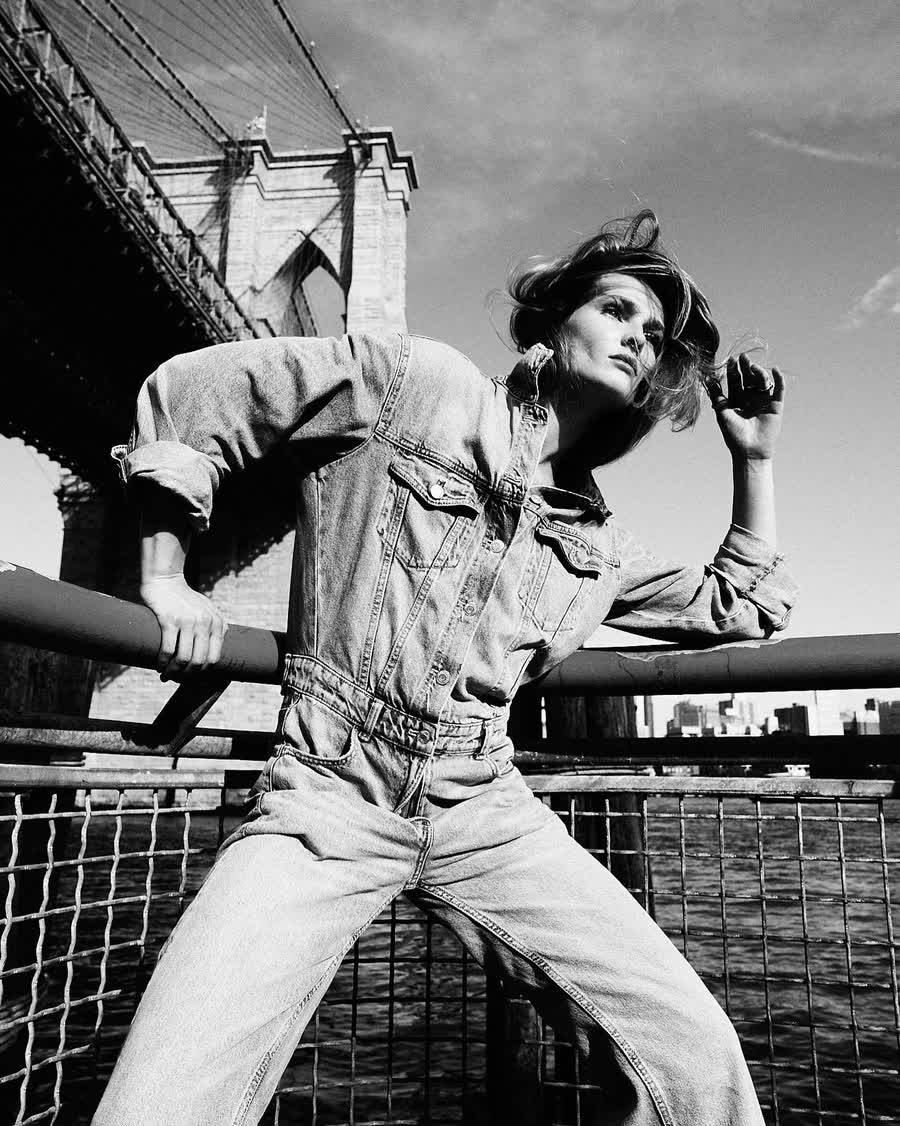 Anastasiia Koval in an oversized denim jacket, leaning against a city railing in black and white.