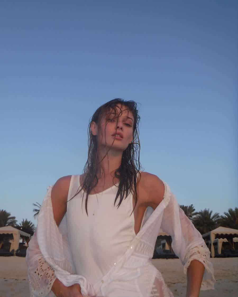 Anastasiia Koval in a white dress on a rooftop under a bright sky.