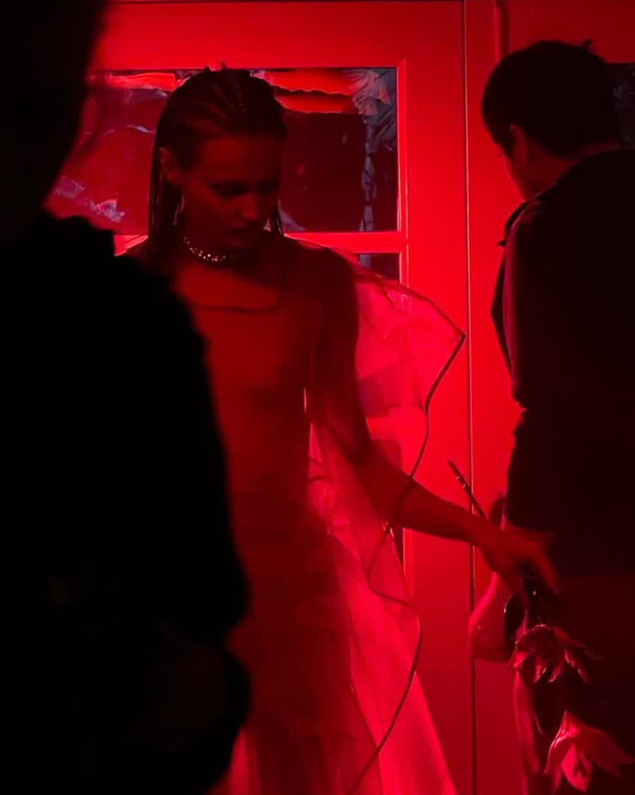 Anastasiia Koval in profile under saturated red light, a sheer jacket over her shoulders.